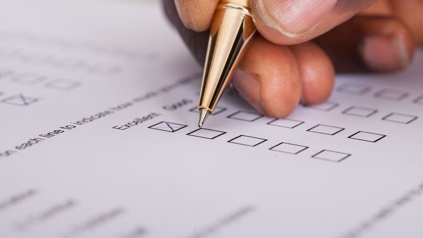 Hand holding a gold pen, marking boxes on a survey paper.