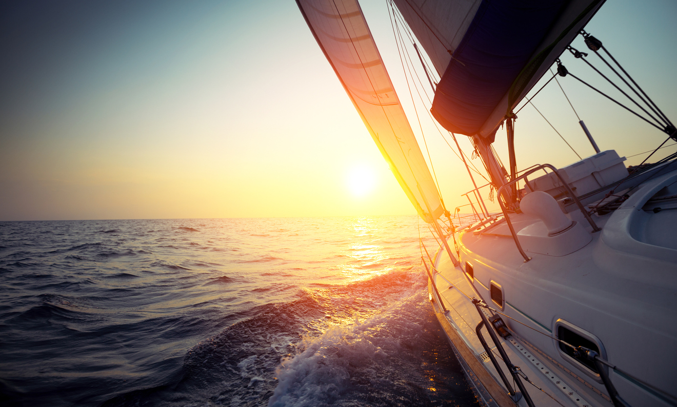 Sail boat gliding in open sea at sunset