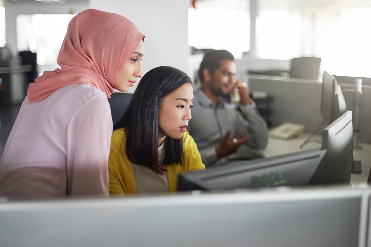 Businesswomen discussing over desktop PC in office. Female colleagues are looking in computer monitor. They are at workplace