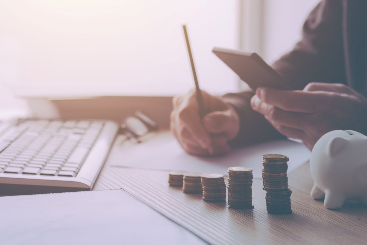 Hands shown woking at desk with coins stacked and piggy bank, budgeting retirement concept