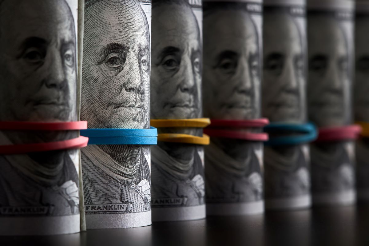 A row of rolled hundred dollar bills with rubber bands on dark background