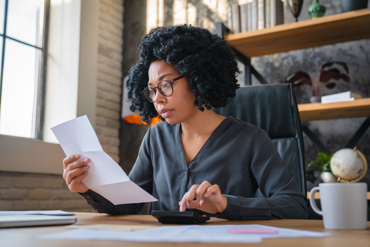 woman calculating finance, money, using calculator, laptop computer at home workplace table